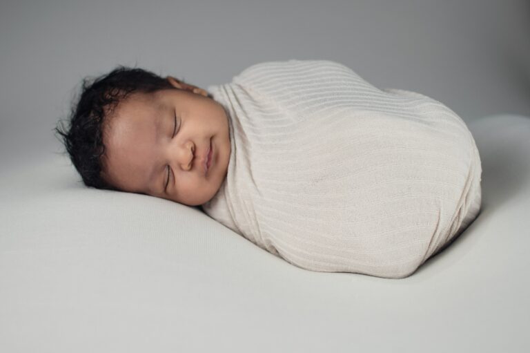 baby in white knit cloth lying on bed